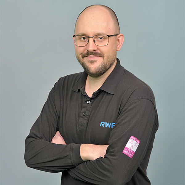 Eine Person in einem schwarzen Vans-Shirt, mit heller Haut, die vor einem grauen Hintergrund steht und Ohrringe trägt. Portrait von Jan Wilke.