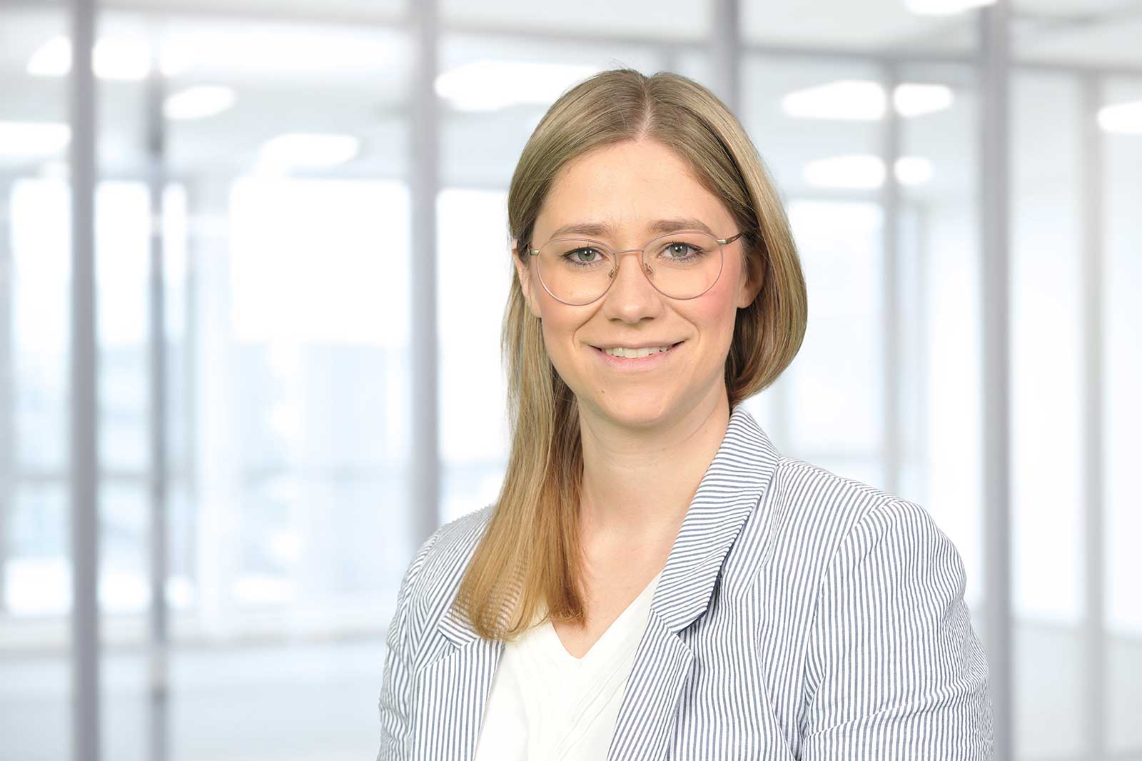 A woman with blonde hair is wearing a striped blazer and standing in a bright, modern office.