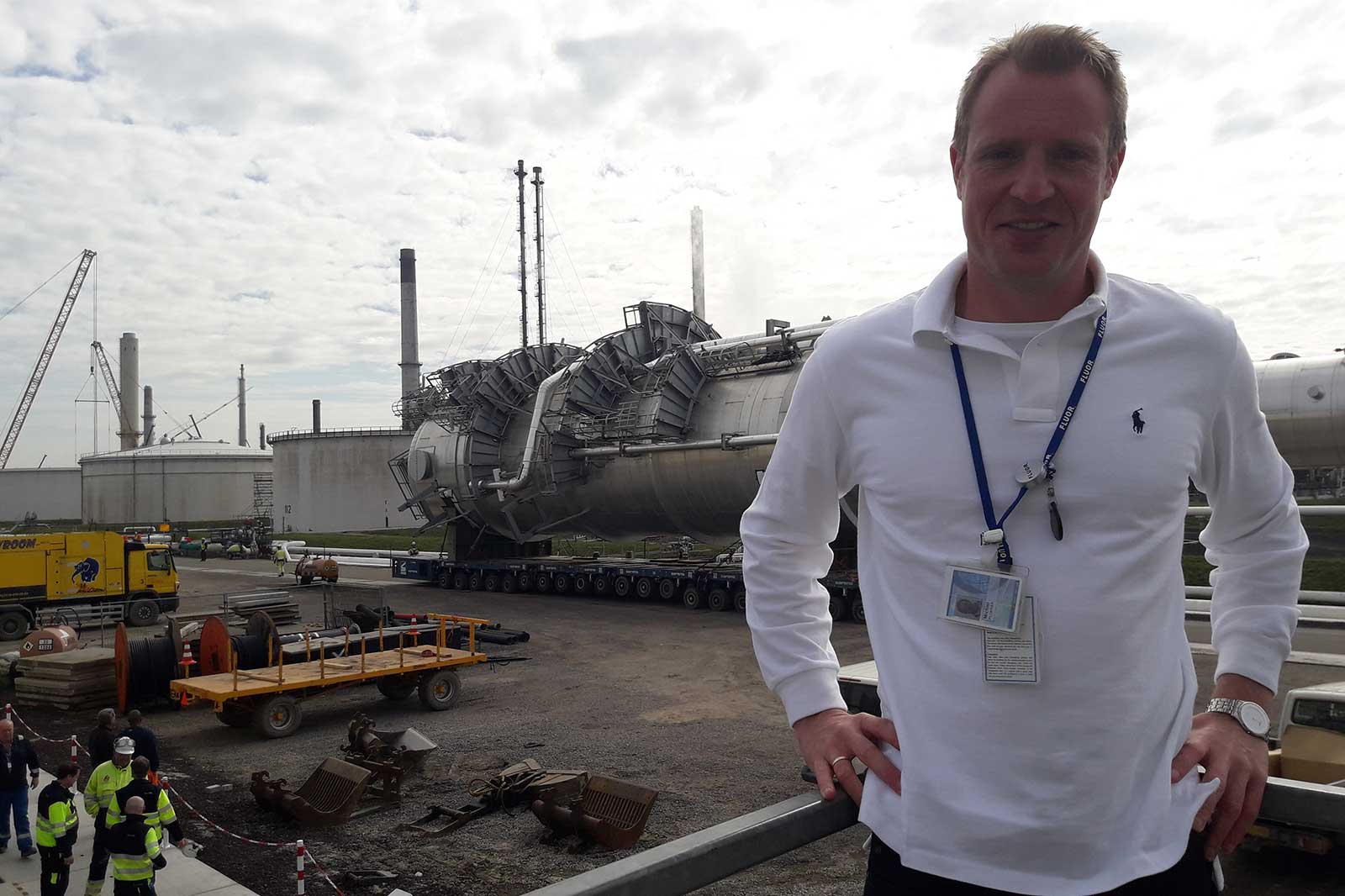 A large industrial tank trailer is on a construction site, surrounded by workers and heavy machinery.