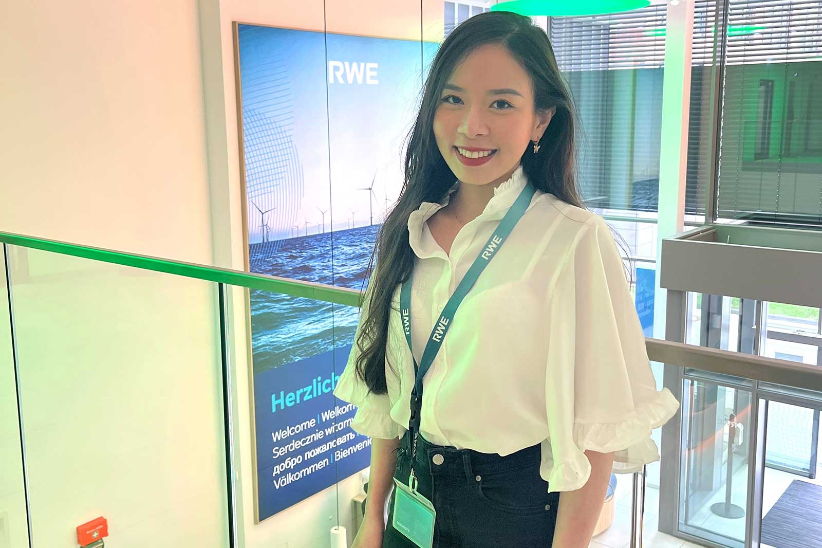 Eine Person steht in einem modernen Raum mit einem RWE-Hintergrund. Sie trägt ein weißes Hemd und eine ID-Karte.