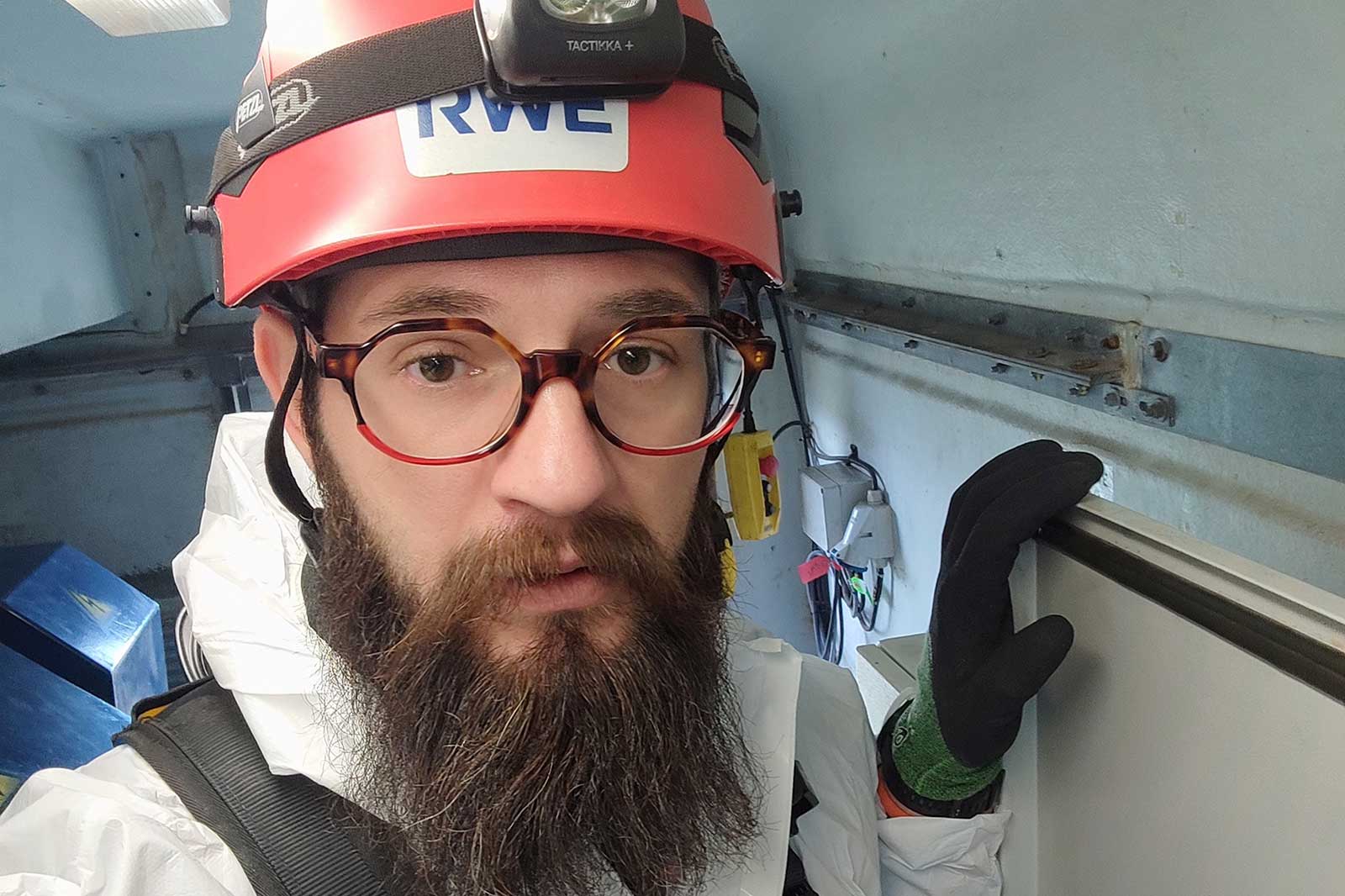 A person wearing an orange helmet with a light is in a grey interior space.