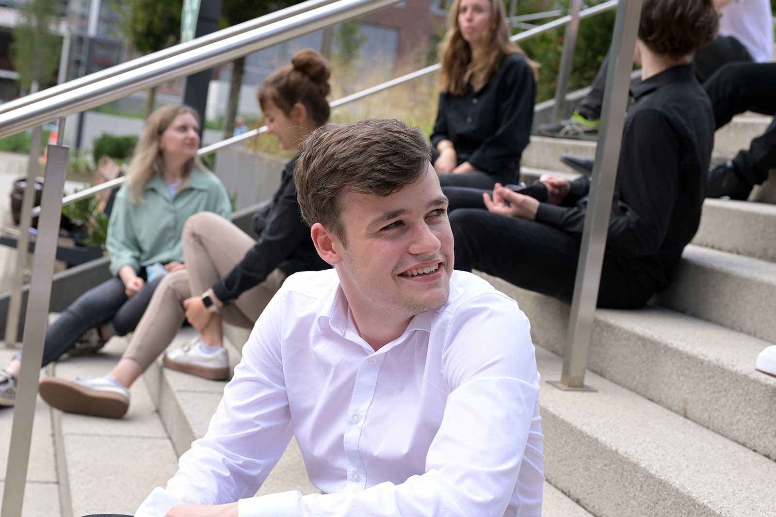 Eine Gruppe junger Menschen sitzt auf Freitreppen und unterhält sich zwanglos miteinander in einer geselligen Umgebung.