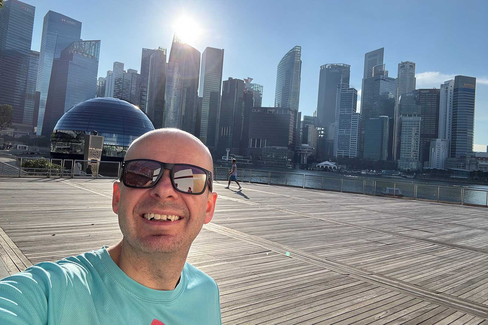 A sunny day at a waterfront promenade with modern skyscrapers in the background and a person walking along the boardwalk.