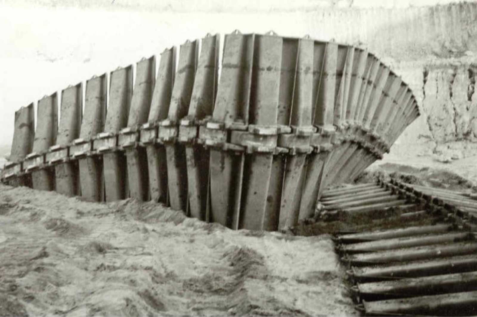 Eine verwitterte Struktur, die einem Schiffsrumpf ähnelt und teilweise im Sand und Schmutz versunken ist.