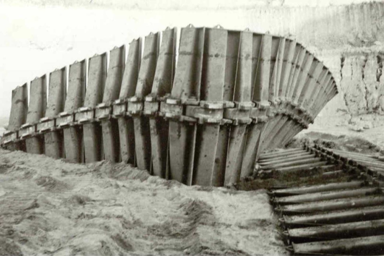 Eine verwitterte Struktur, die einem Schiffsrumpf ähnelt und teilweise im Sand und Schmutz versunken ist.