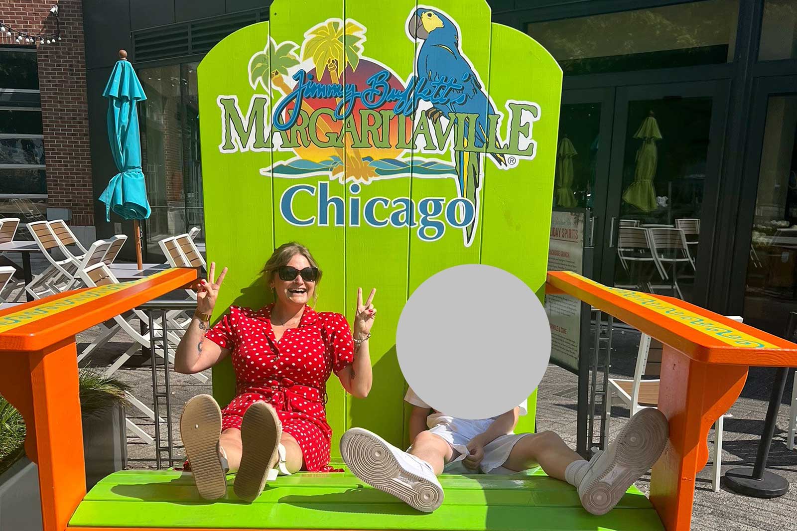 Eine Frau in einem roten gepunkteten Kleid und ein Kind sitzen auf einem großen, hellgrünen Stuhl mit dem Schild 'Margaritaville Chicago'.
