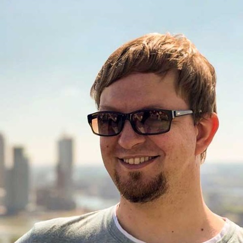 Eine Person mit Brille steht im Freien vor einer Stadtsilhouette und genießt einen sonnigen Tag.