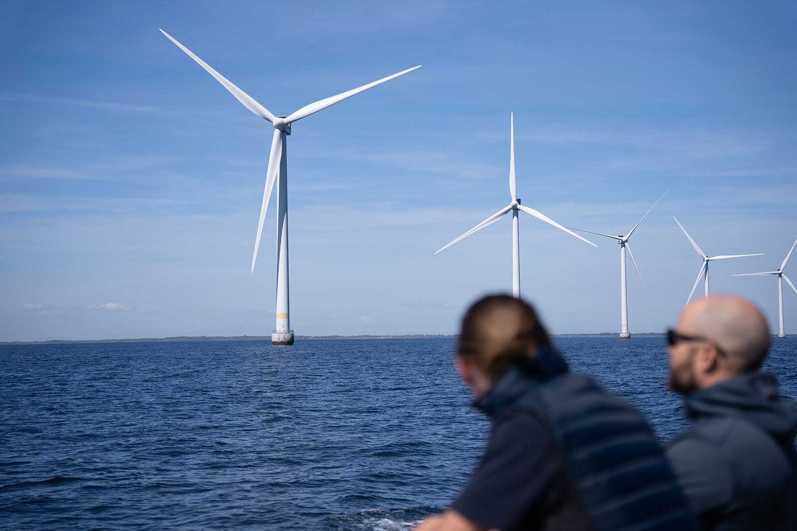 Der Blick auf mehrere Windkraftanlagen, die im Wasser stehen, während zwei Personen auf einem Boot sitzen.