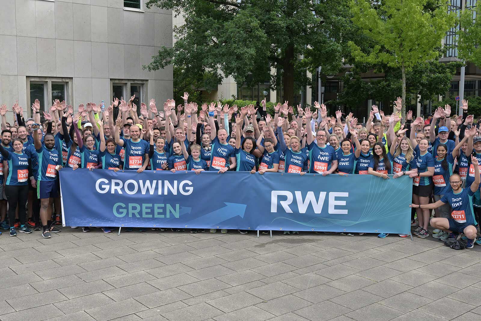 A group of runners raises their hands in front of a banner reading 'GROWING GREEN' and 'RWE'.