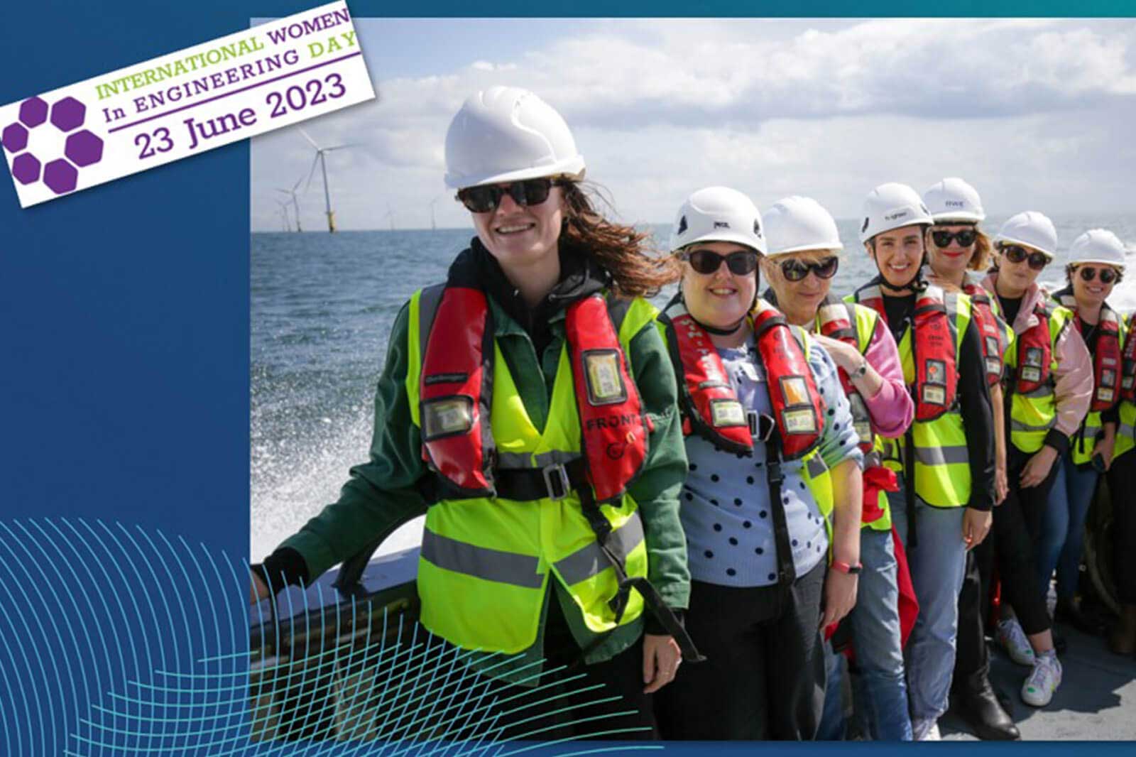 Eine Gruppe von Frauen in Sicherheitswesten und Helmen auf einem Boot, mit Windkraftanlagen im Hintergrund. Internationaler Frauentag in Ingenieurwesen.