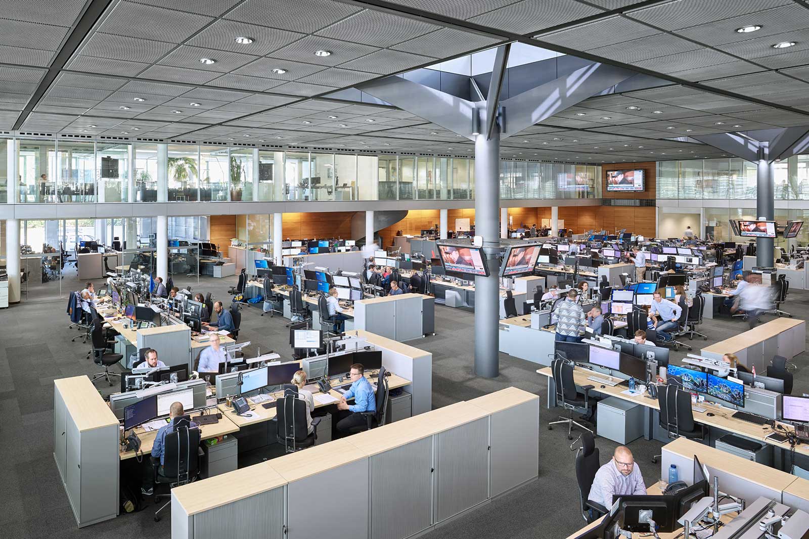A modern office space featuring multiple workstations, computer screens, and employees engaged in their tasks.