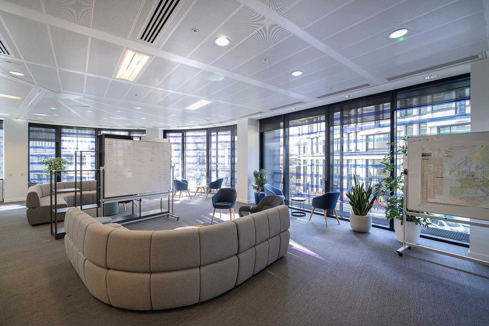 Modern office space featuring a curved sofa, whiteboard, and large windows. Bright, inviting atmosphere with plants.