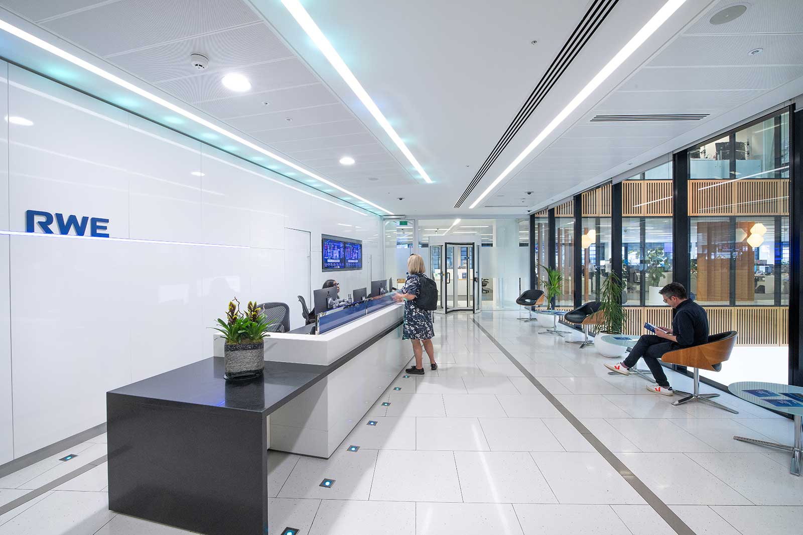 A modern reception area featuring a reception desk, plants, and seating areas, all brightly lit.