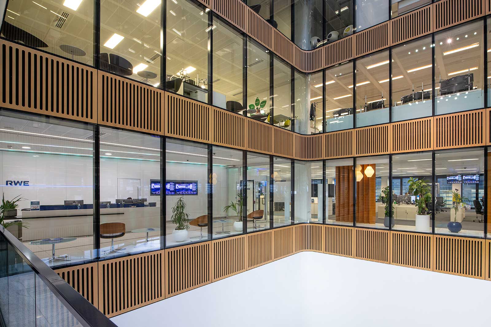 The image features a modern office space with large windows and wooden paneling. Plants and office furniture are visible.