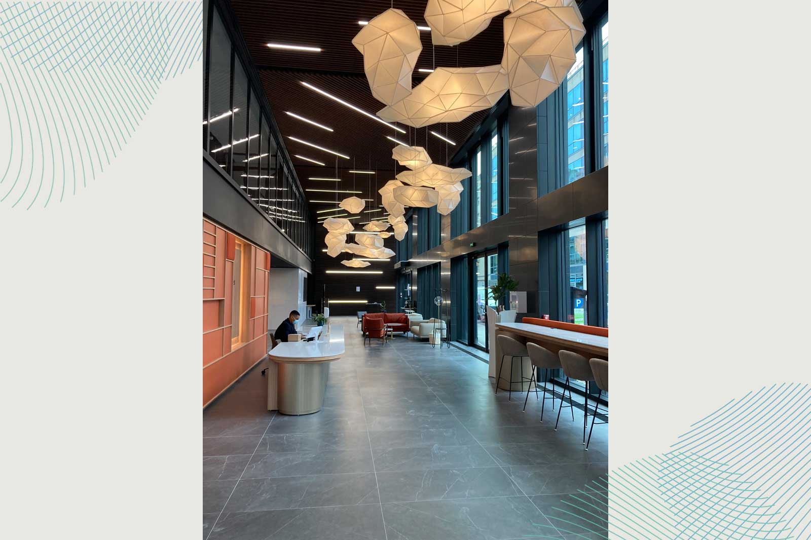 Modern reception area with geometric light fixtures, reception desk, and seating areas. Bright, open atmosphere.