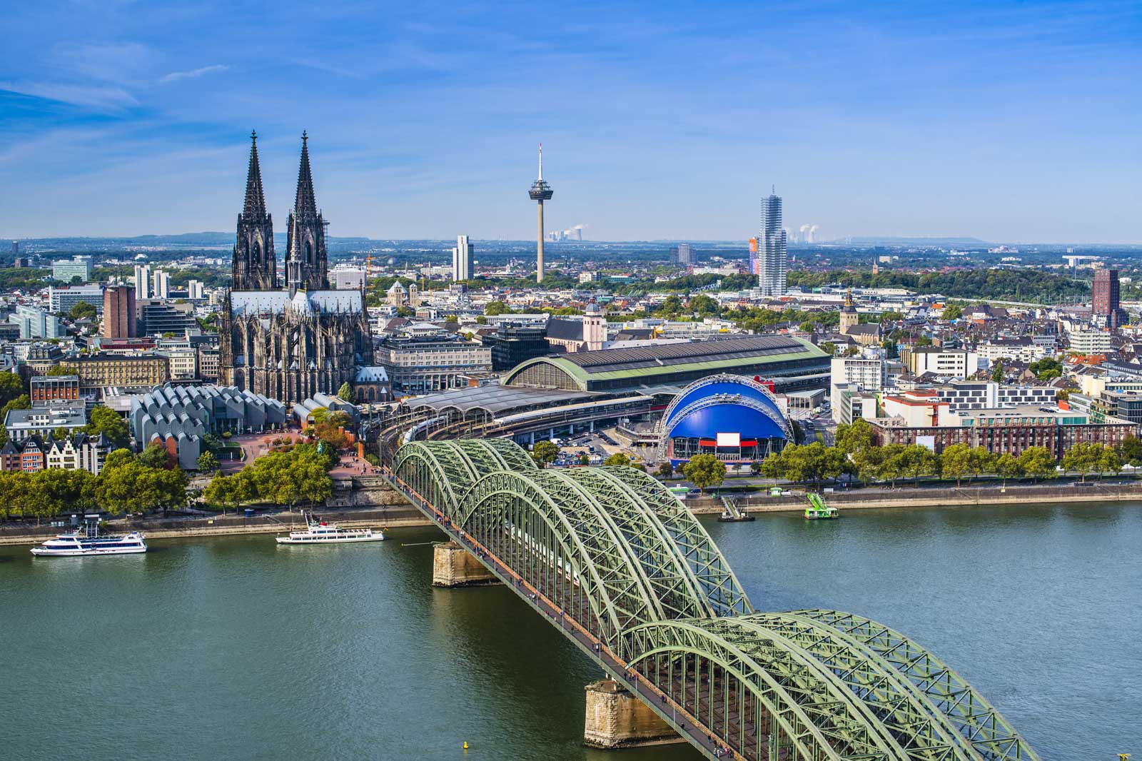 Kölner Skyline mit dem Kölner Dom und der Hohenzollernbrücke über dem Rhein an einem sonnigen Tag.
