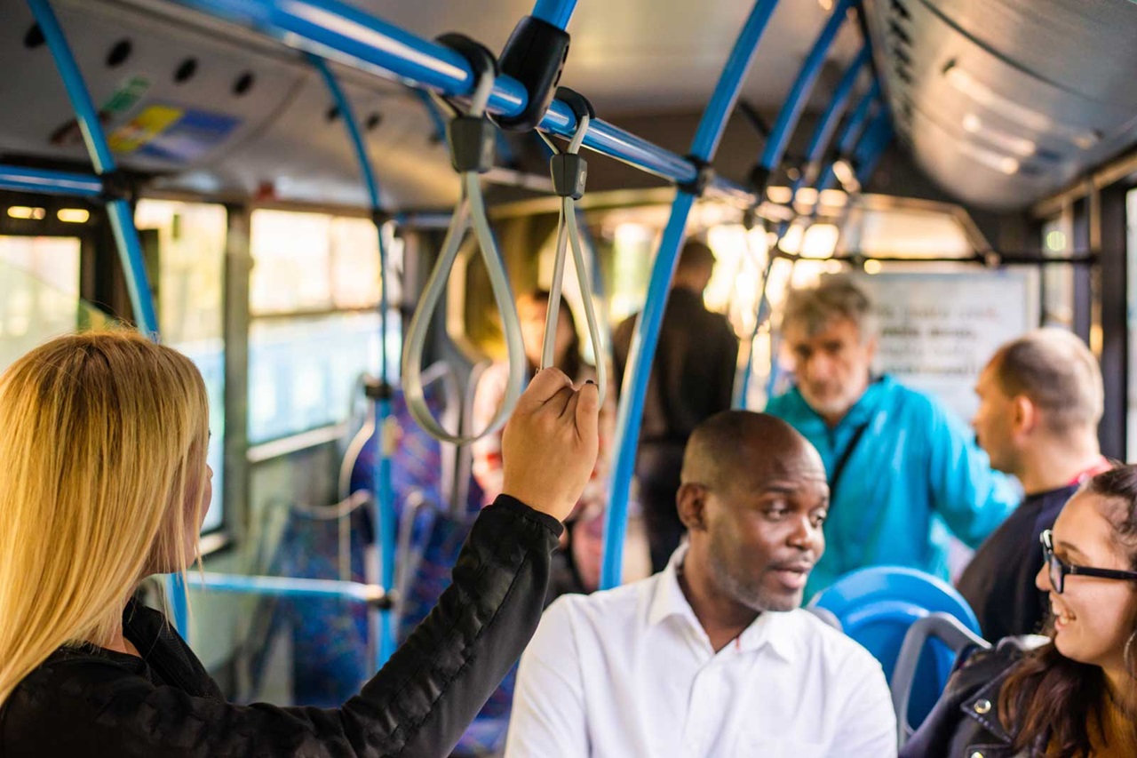 A person is holding onto a handrail in a bus while other passengers are seated.