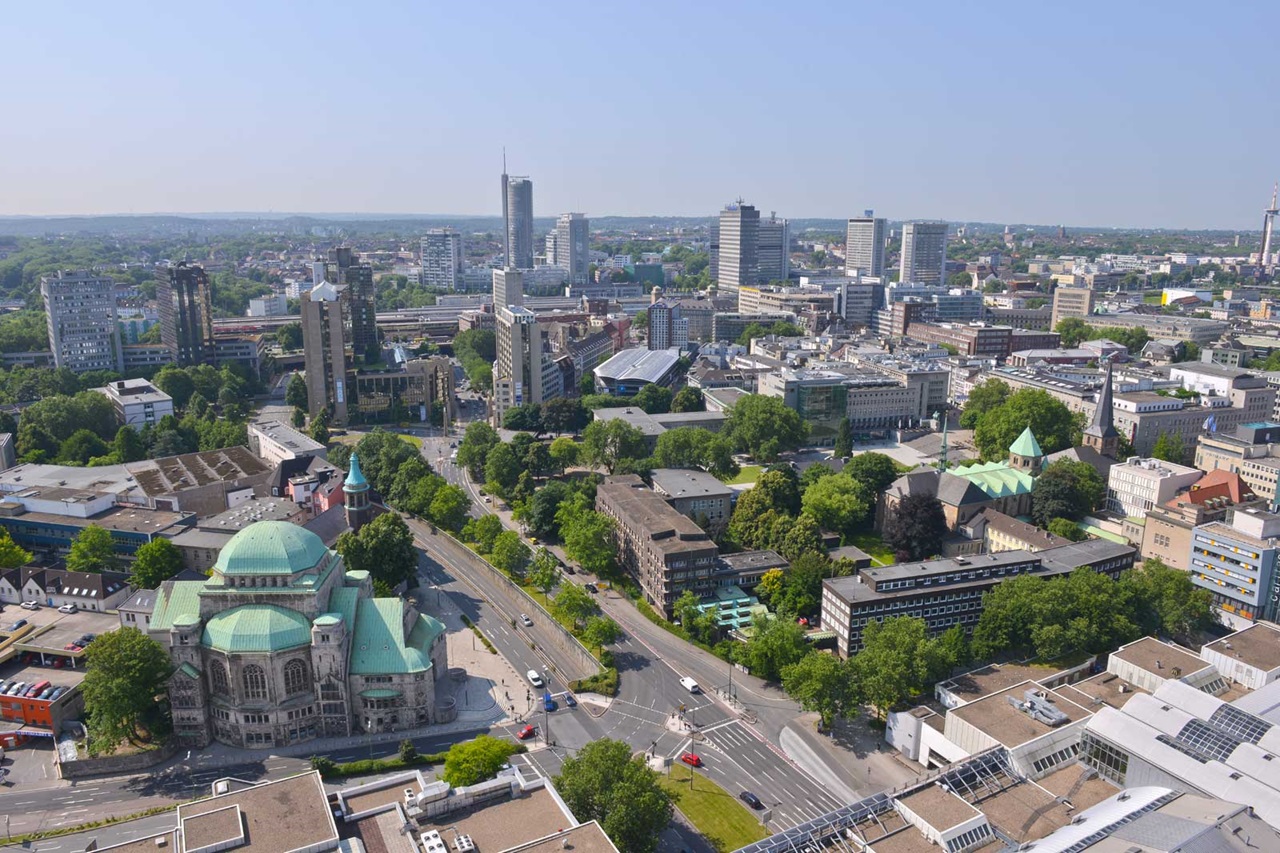 Aerial view of a modern city with green spaces, buildings, and a notable domed structure with green roofing.