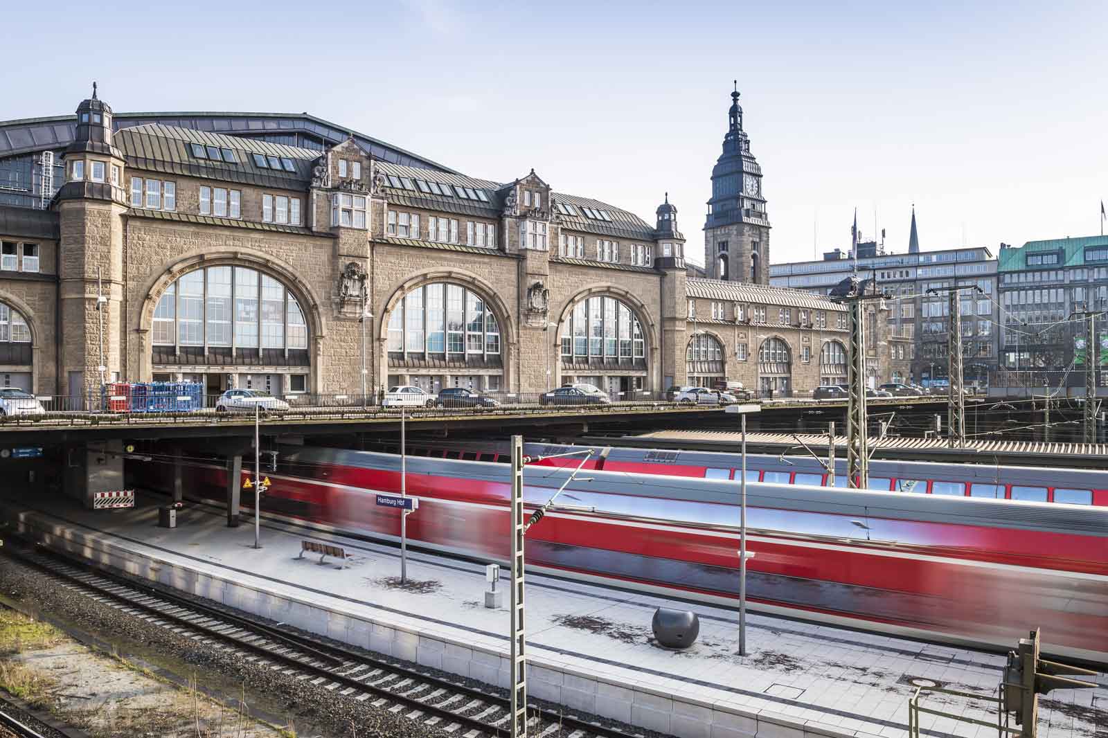 A historic railway station featuring stunning architecture, with a red train passing by.