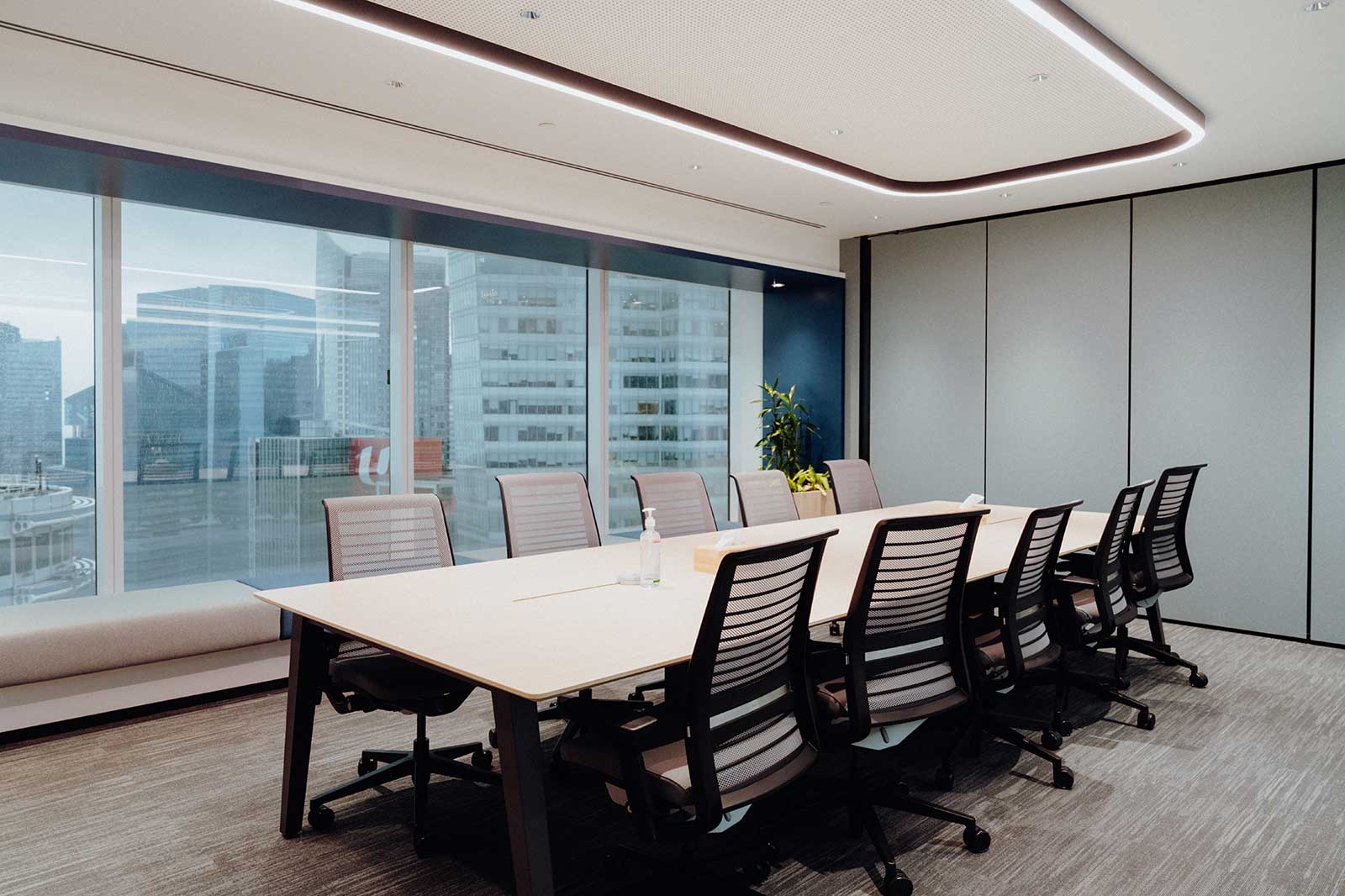 A modern meeting room featuring a long table, chairs, and large windows offering a view of the city skyline.