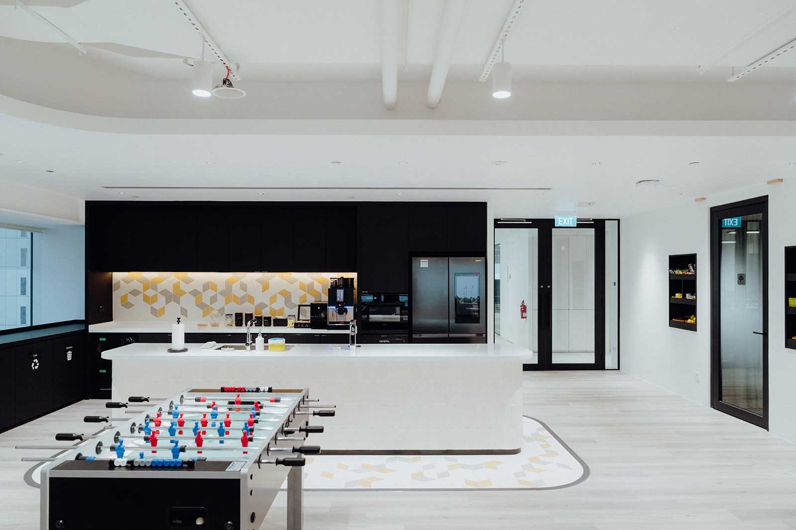 Modern office kitchen featuring a foosball table, a sleek kitchen countertop, and bright, minimalist furnishings.