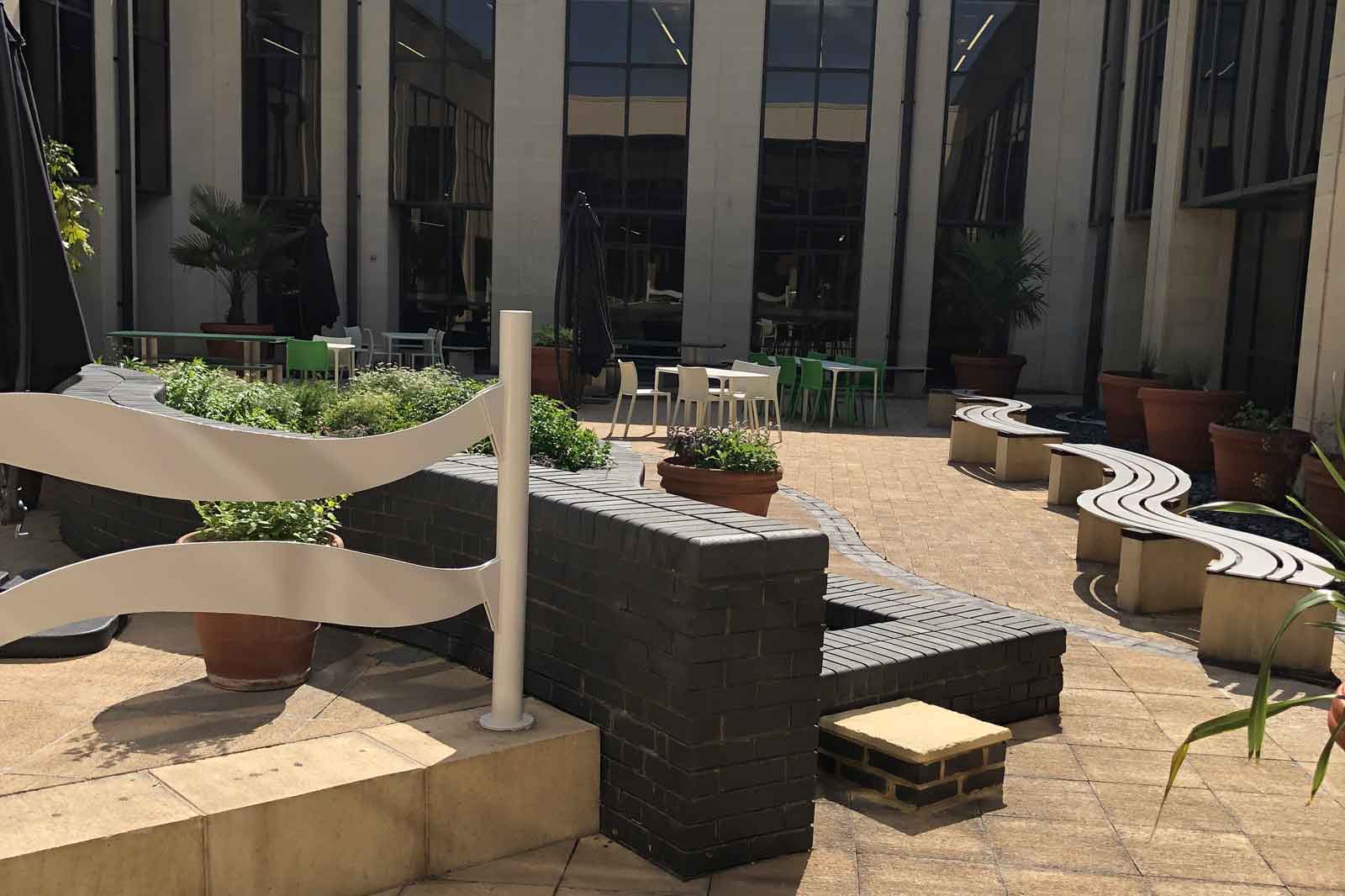 An indoor courtyard featuring furniture. Green grass and potted plants surround a curved bench and a brick wall.