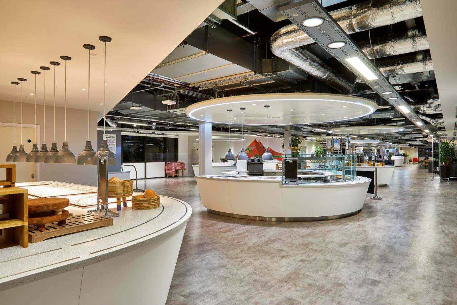 A modern dining area featuring circular counters, hanging lights, and a bright, open space. Plants are visible in the background.