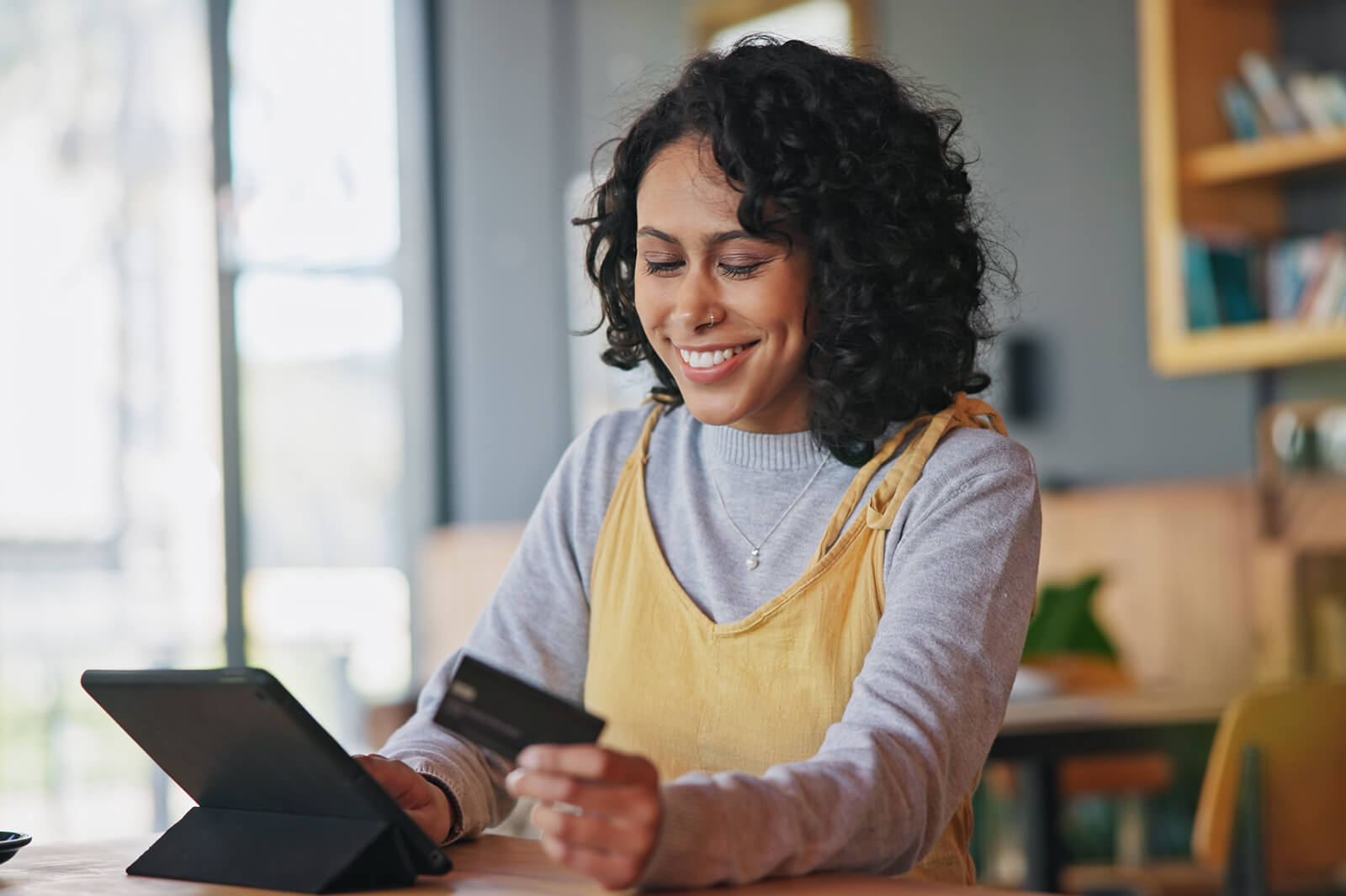 A person seated at a table using a tablet and holding a credit card in a modern cafe setting.